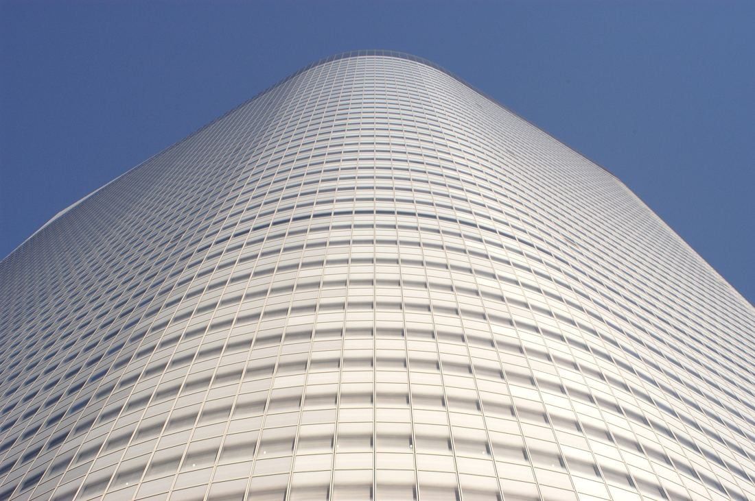 Looking up the curved glass facade of a tall office tower against a deep blue sky
