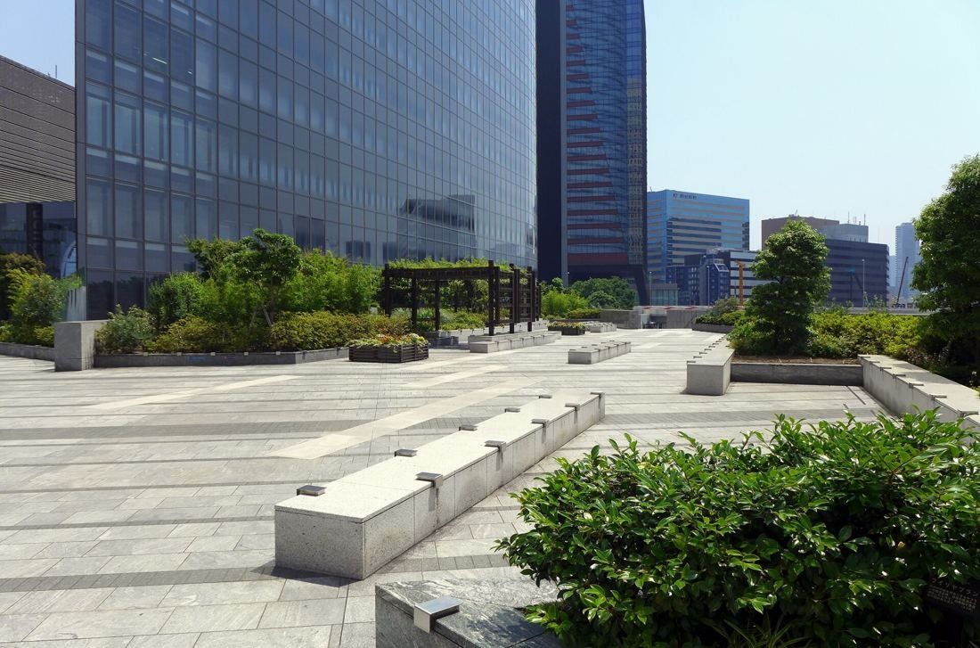 Dentsu: Paved open plaza with planting and benches beside the glass base of the tower