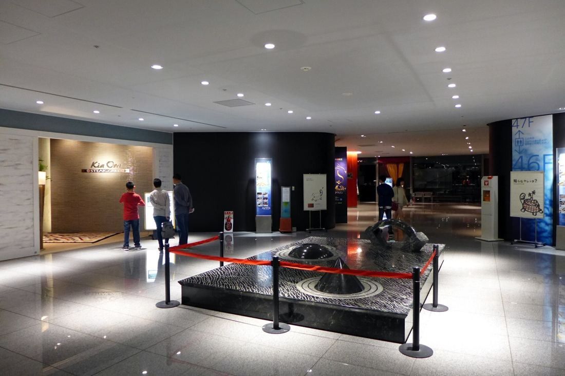 Dentsu: Polished stone lobby with a black sculpture fountain and restaurant entrances