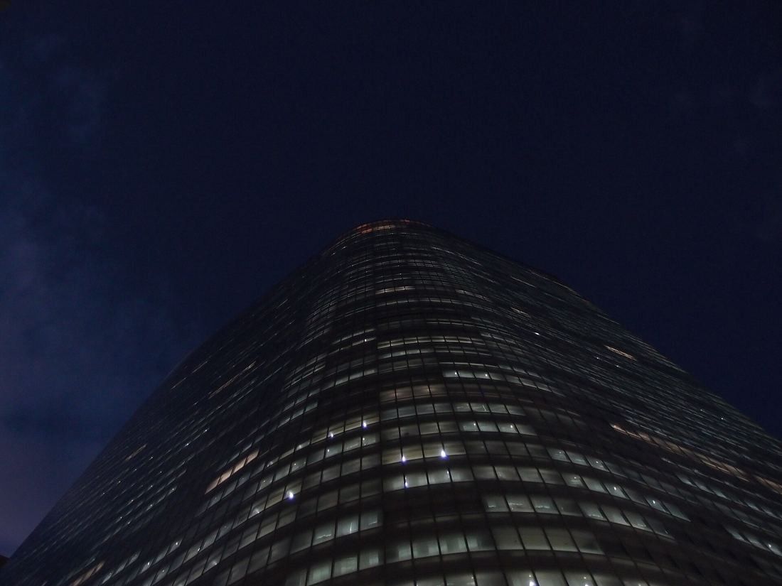 Dentsu: The rounded top of a glass tower lit floor by floor at night