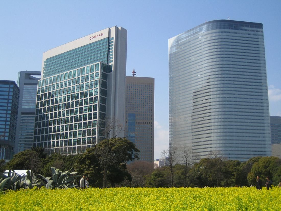 Dentsu: Two glass towers rising behind a garden with a yellow flower field