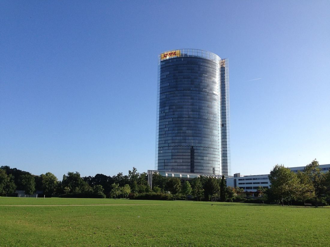 DHL Group: Elliptical glass tower above a wide green lawn under blue sky