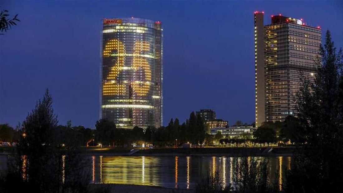 DHL Group: Tower lit with a large number 25 at night, reflected in water