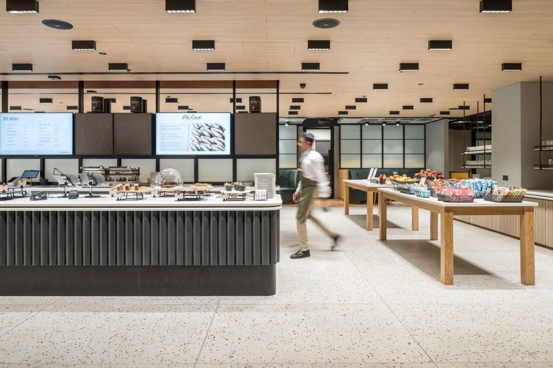 Diageo: Food counter with menu screens, a pale terrazzo floor and wooden tables of snacks and fruit
