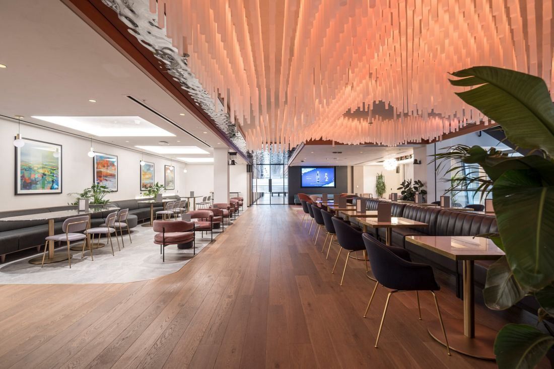 Diageo: Long dining space with banquettes, small tables and a sculptural slatted ceiling in warm light