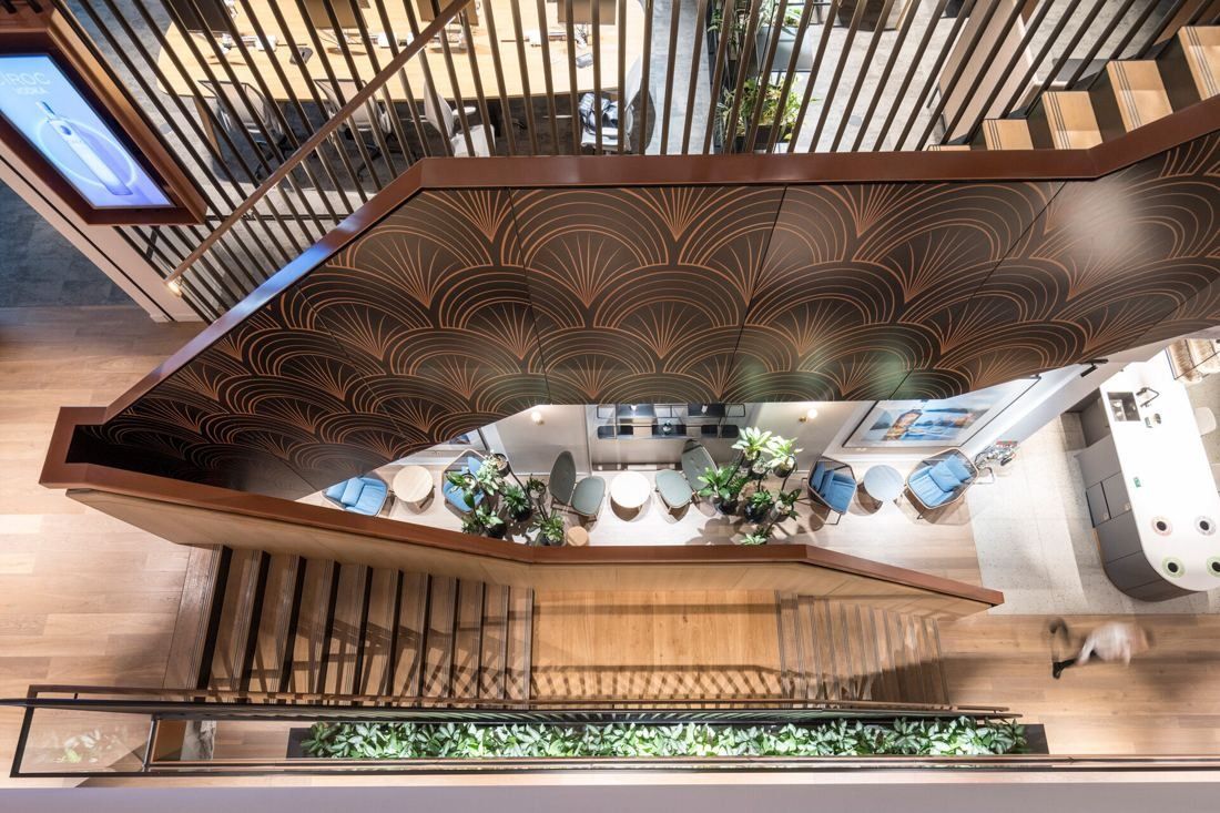 Diageo: Looking down a timber staircase with a patterned wooden soffit into a planted lounge below