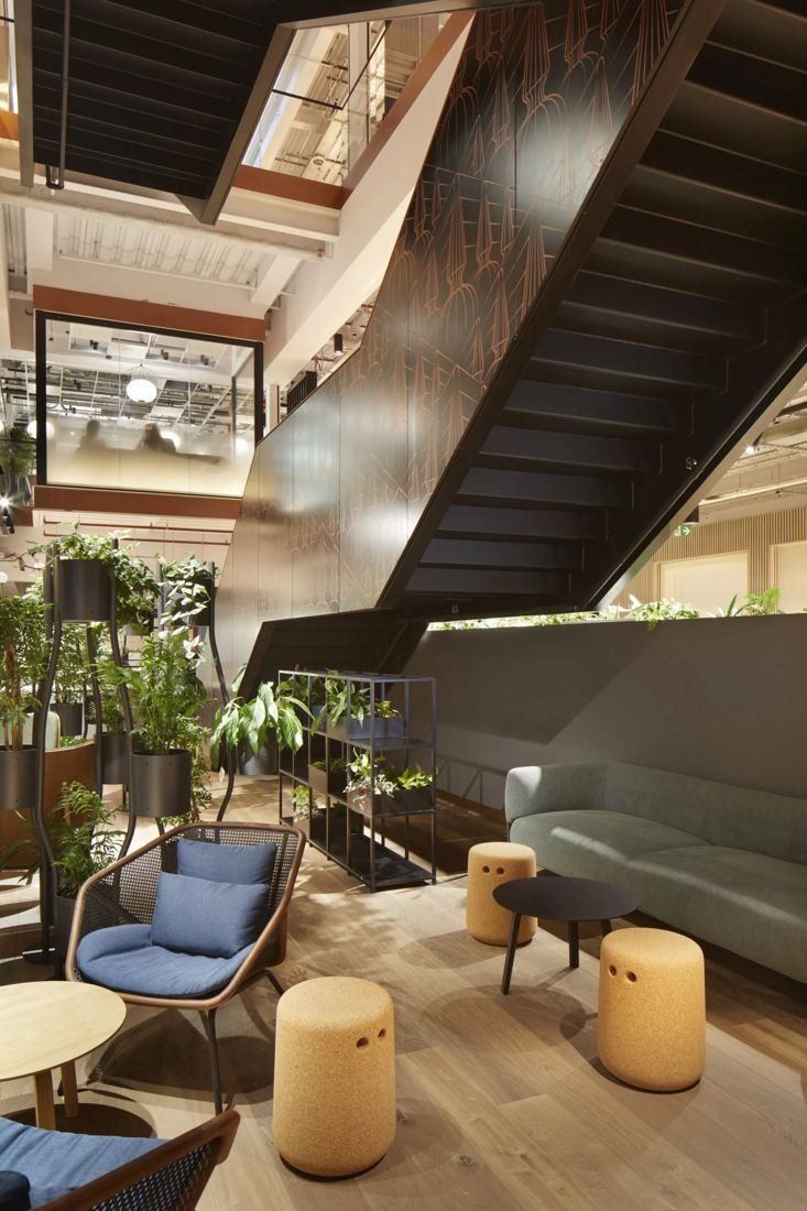 Diageo: Lounge with armchairs, cork stools and plants beneath a dark steel staircase
