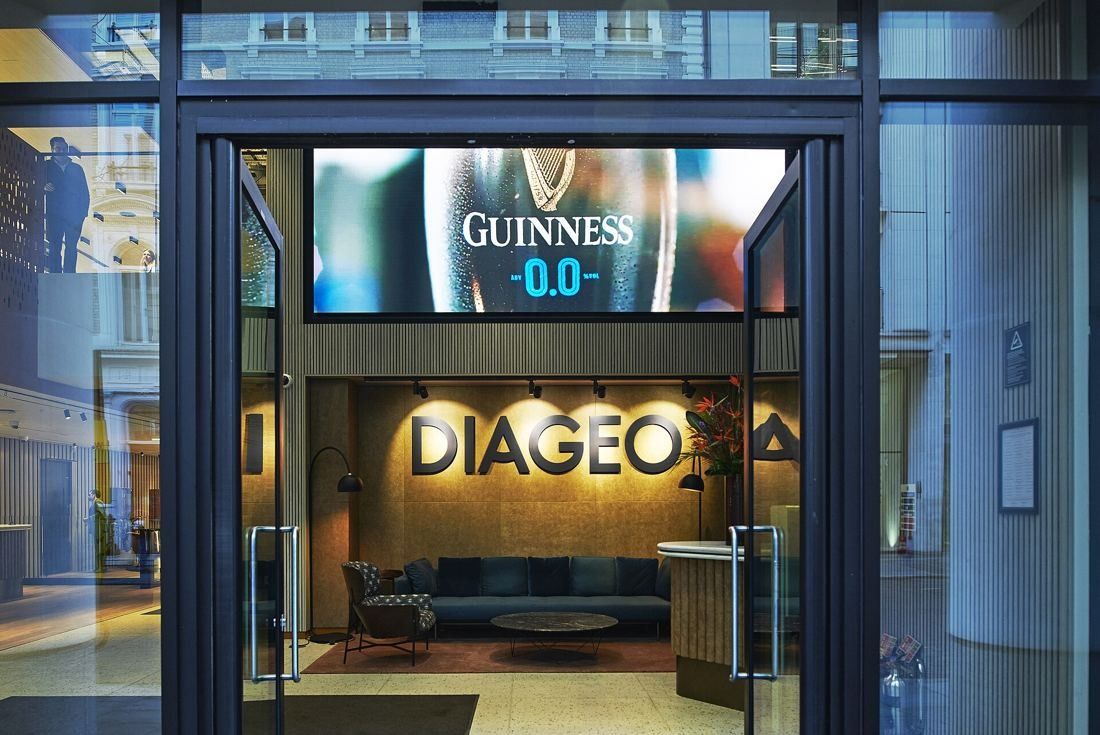 Diageo: Open glass doors into a reception with a large wall sign, a sofa and a screen above