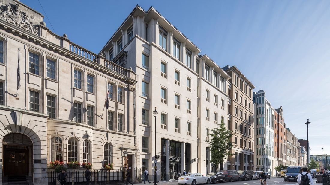 Pale stone office building with a colonnaded ground floor on a sunny London street, between older stone and brick buildings