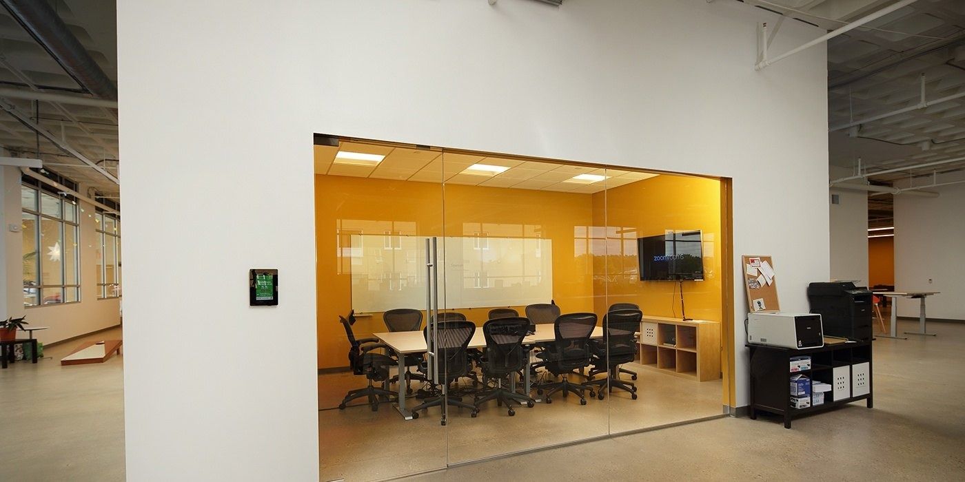 Duolingo: Glass-walled meeting room with an orange wall, a long table and black chairs