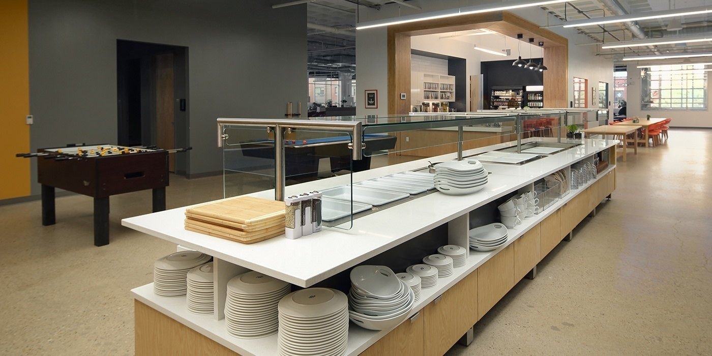 Duolingo: Long buffet counter with stacked plates and a foosball table nearby