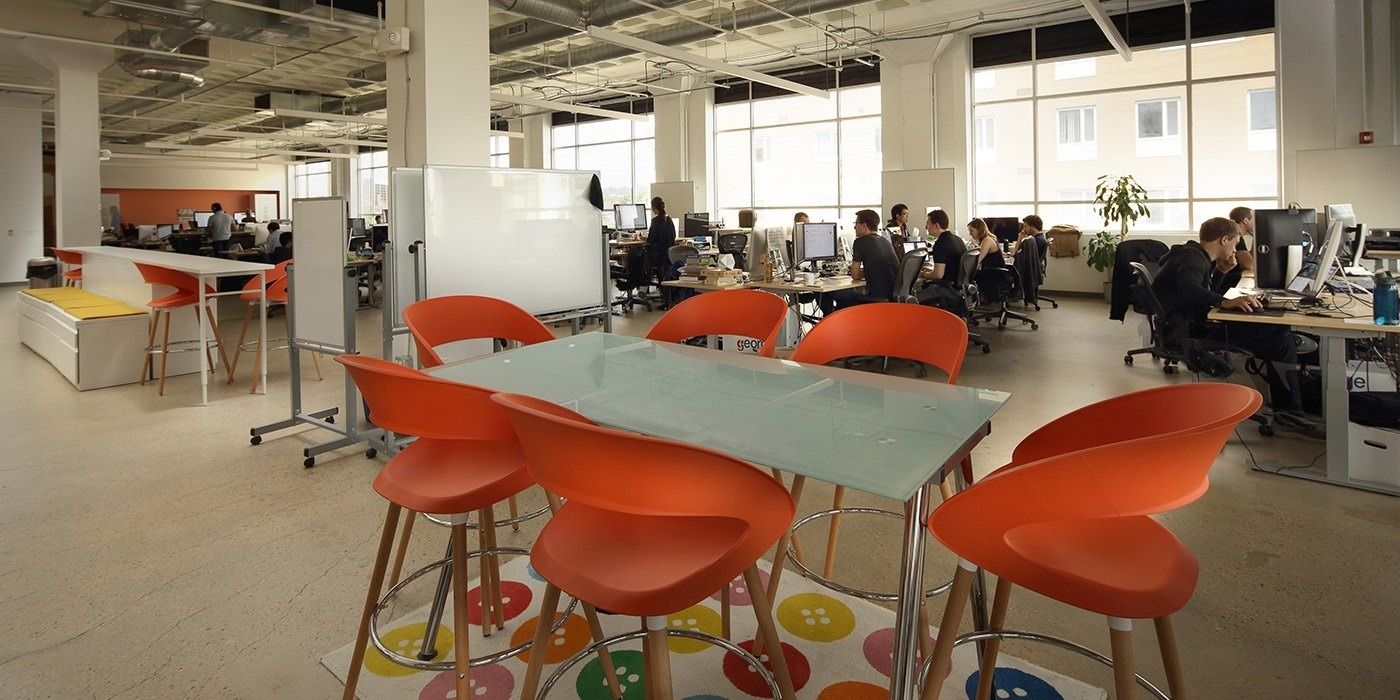 Duolingo: Orange stools around a glass table on a dotted rug, with desks behind