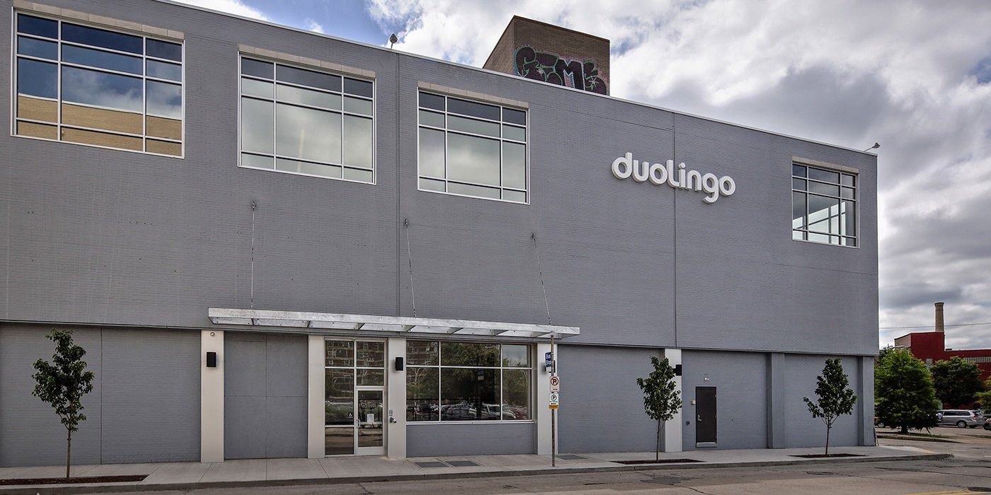 Two-story gray building with large windows and a duolingo sign on the facade