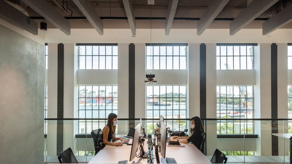 Dyson: Desks with monitors in front of tall industrial windows looking out over the water