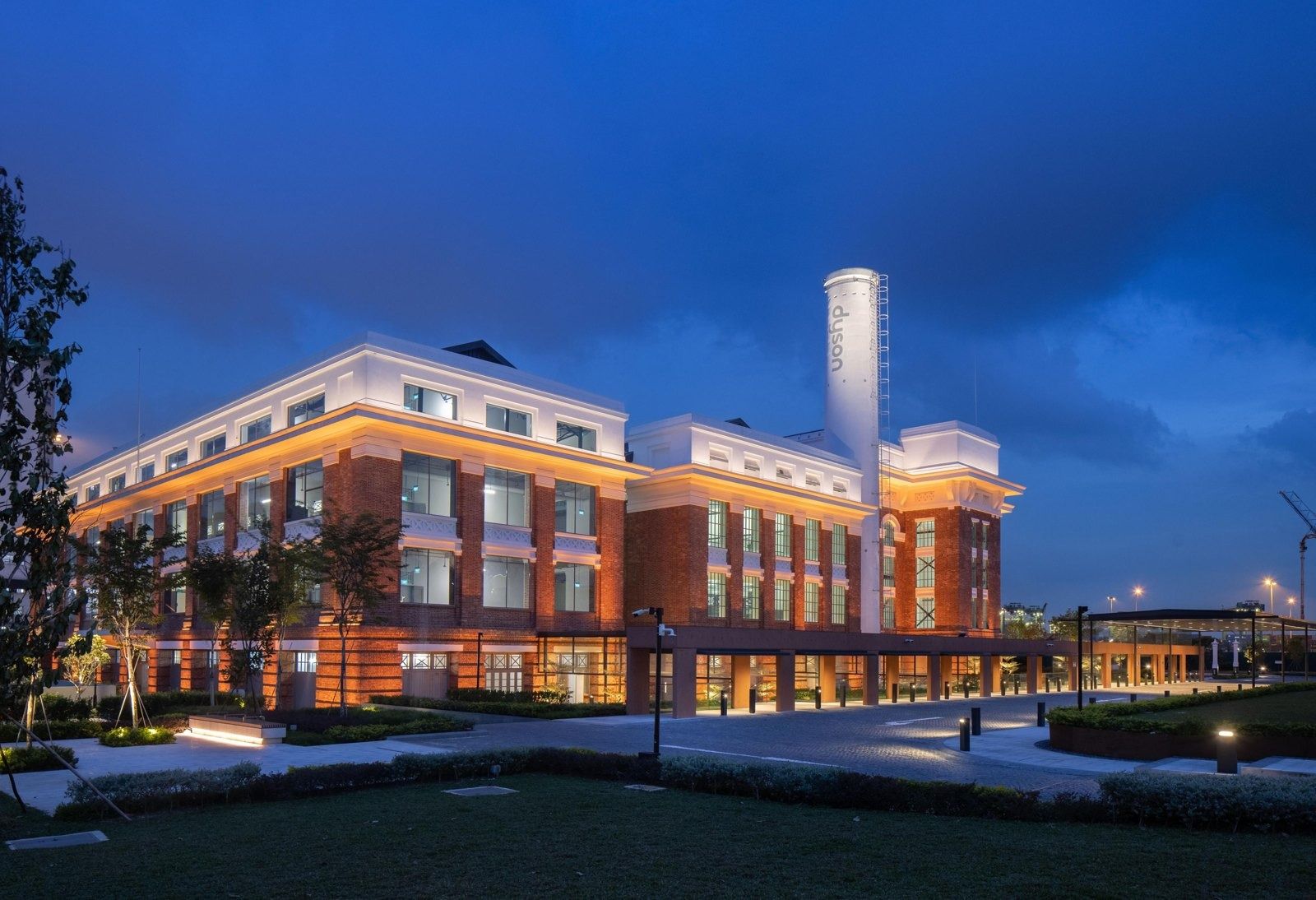 Dyson: Red-brick building with white chimney lit in orange at dusk, with a long covered walkway