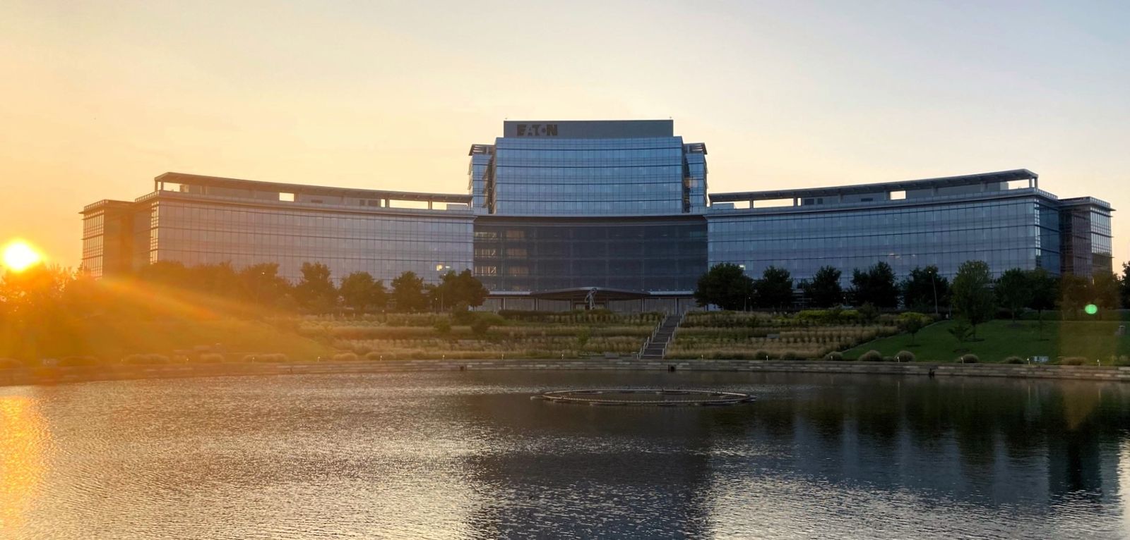 Eaton: A curved glass office building across a pond with the sun low behind it