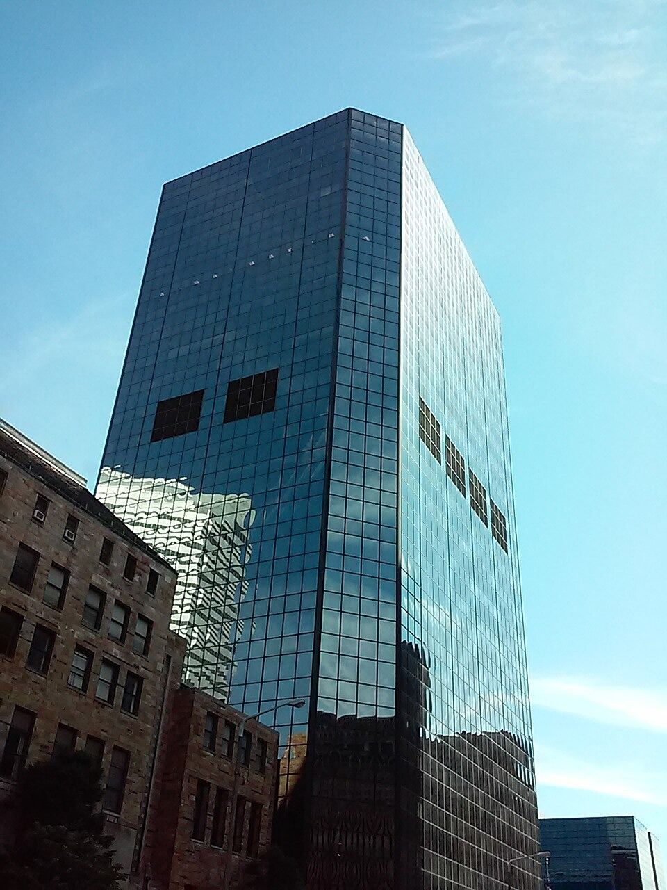 A dark glass office tower seen from street level beside older brick buildings