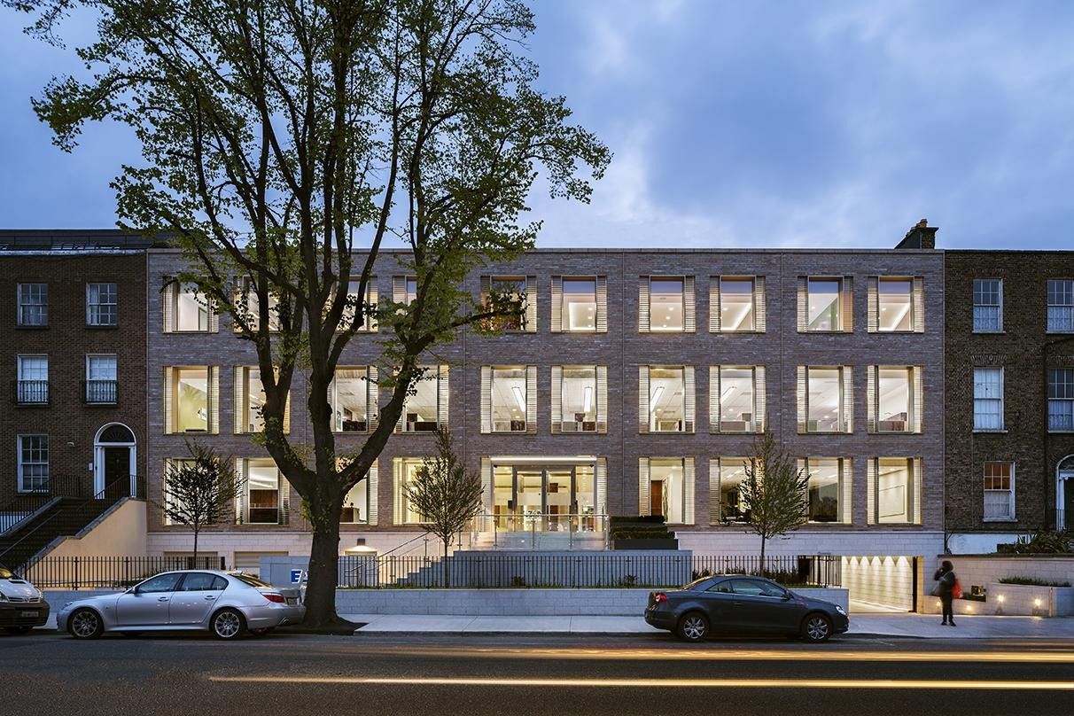 A long brick-and-glass office front lit at dusk behind street trees