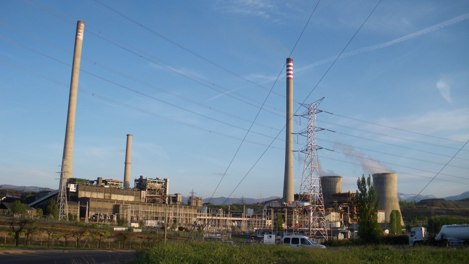 A coal-fired power station with tall chimneys and cooling towers in hilly countryside
