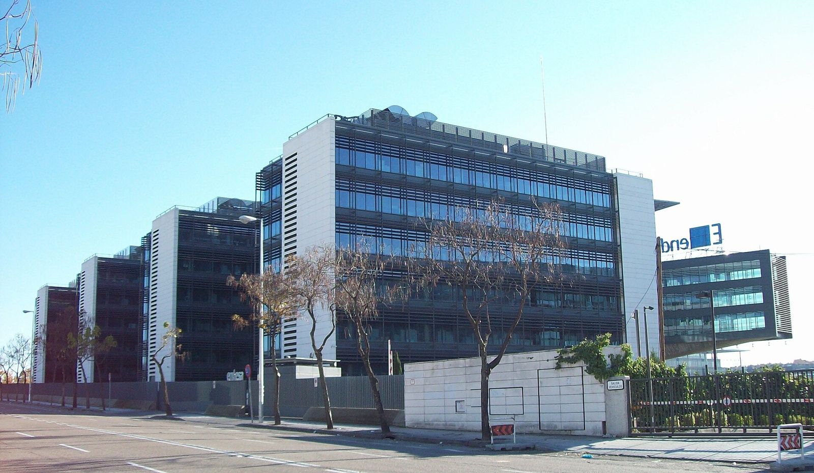 Endesa: A corner office wing with a glass stair tower and a solar canopy above