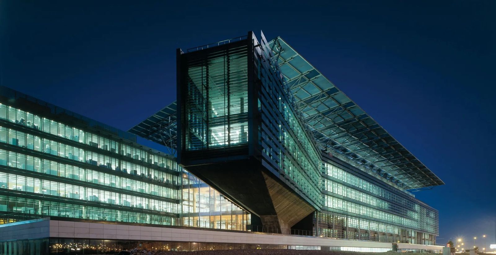 A glass office block with a cantilevered corner lit up against a deep blue evening sky