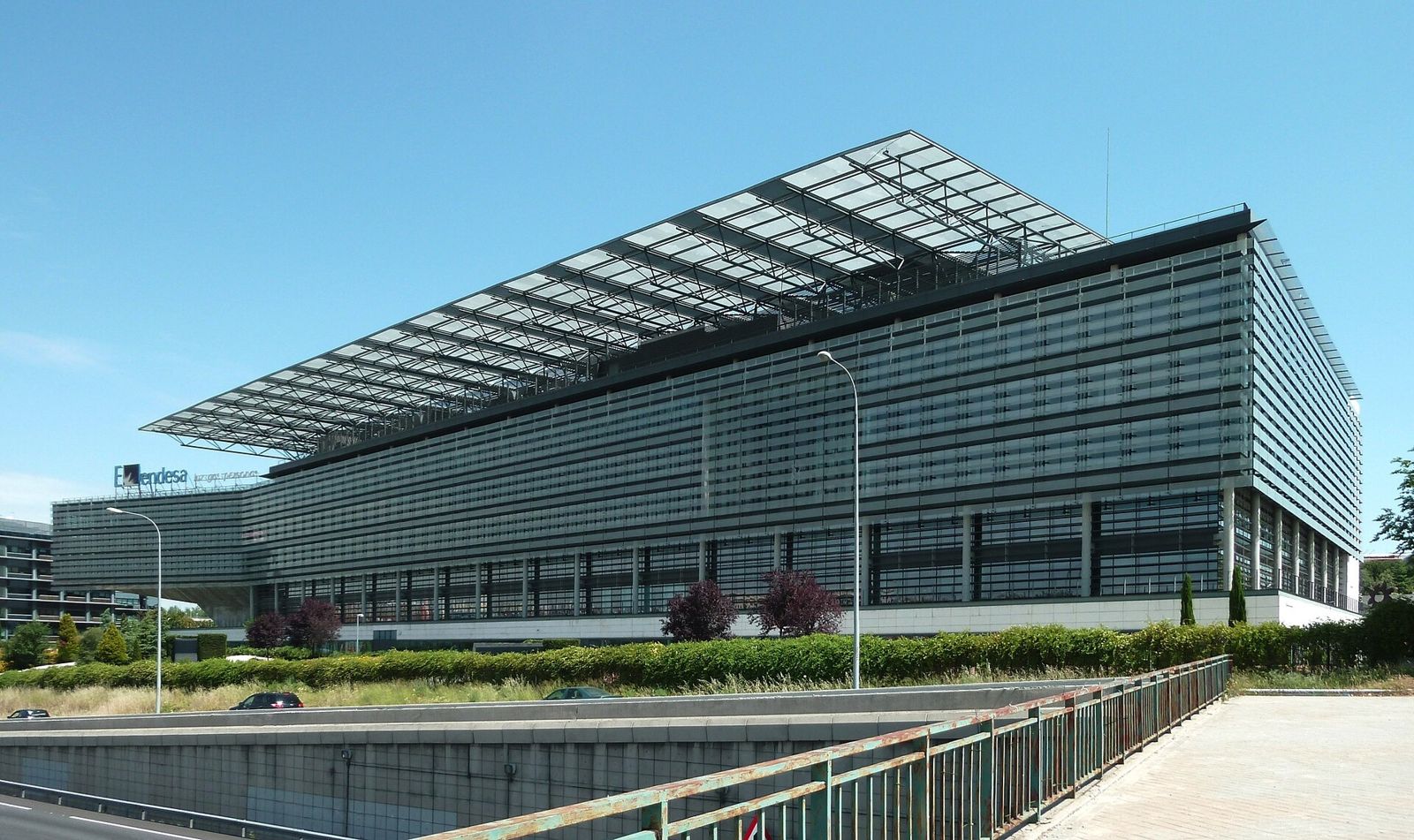 Endesa: A long glass office building with a sloping canopy of panels beside a pool