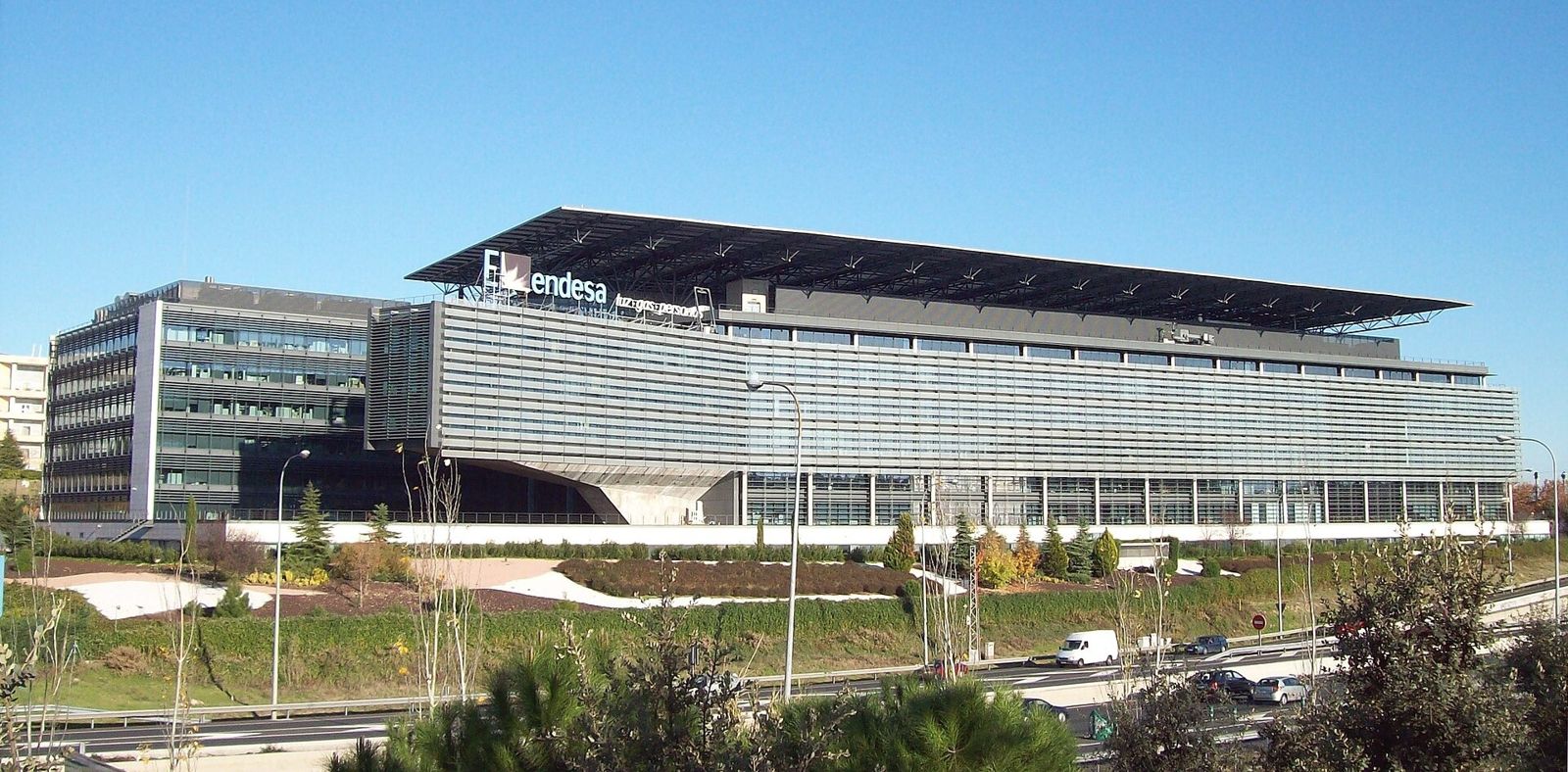 Endesa: A low glass building under a large roof canopy beyond landscaped slopes