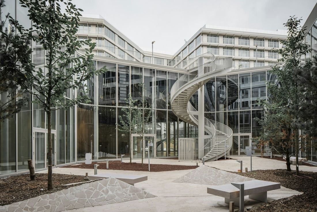 ENGIE: Glass courtyard façade with an external spiral staircase, young trees and stone benches