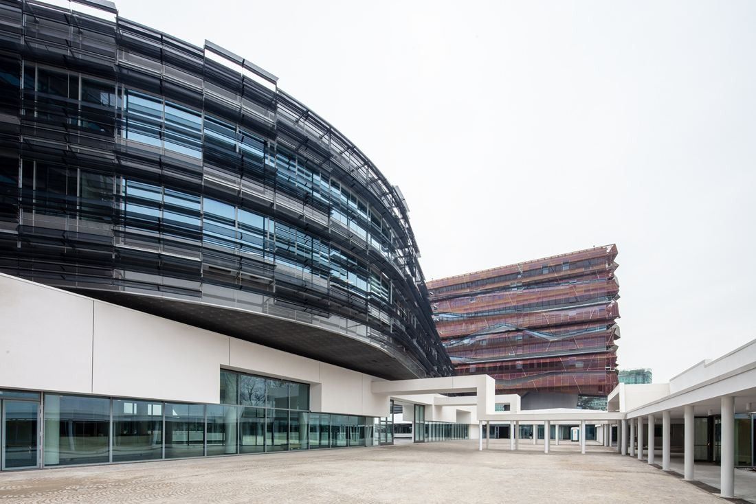 Eni: A curved dark glass building with a bronze-toned tower behind a white plaza