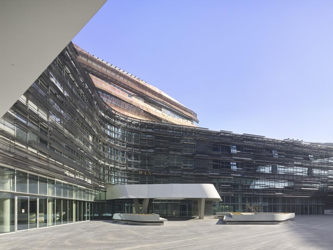 Eni: A curving glass and metal facade above a broad paved terrace