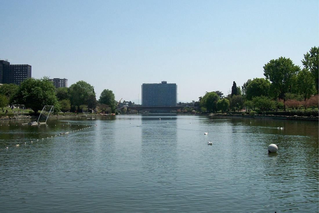 Eni: A distant glass tower at the end of a wide lake with buoys and trees
