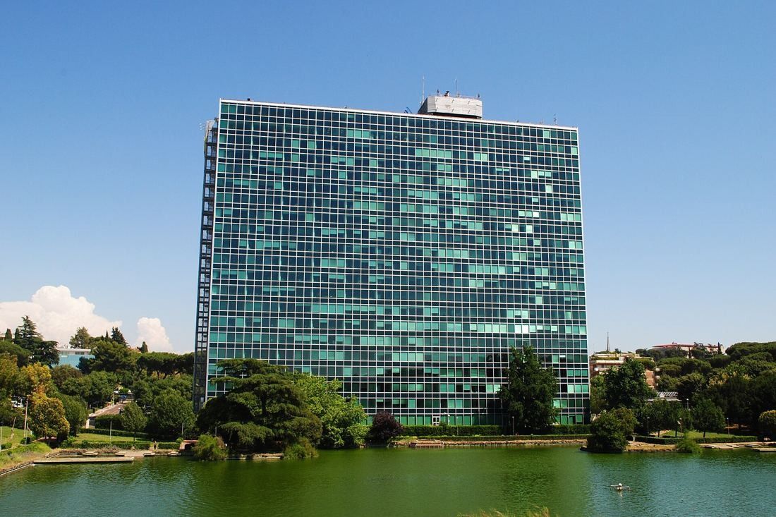 Eni: A glass curtain-wall tower behind trees on the edge of a green lake