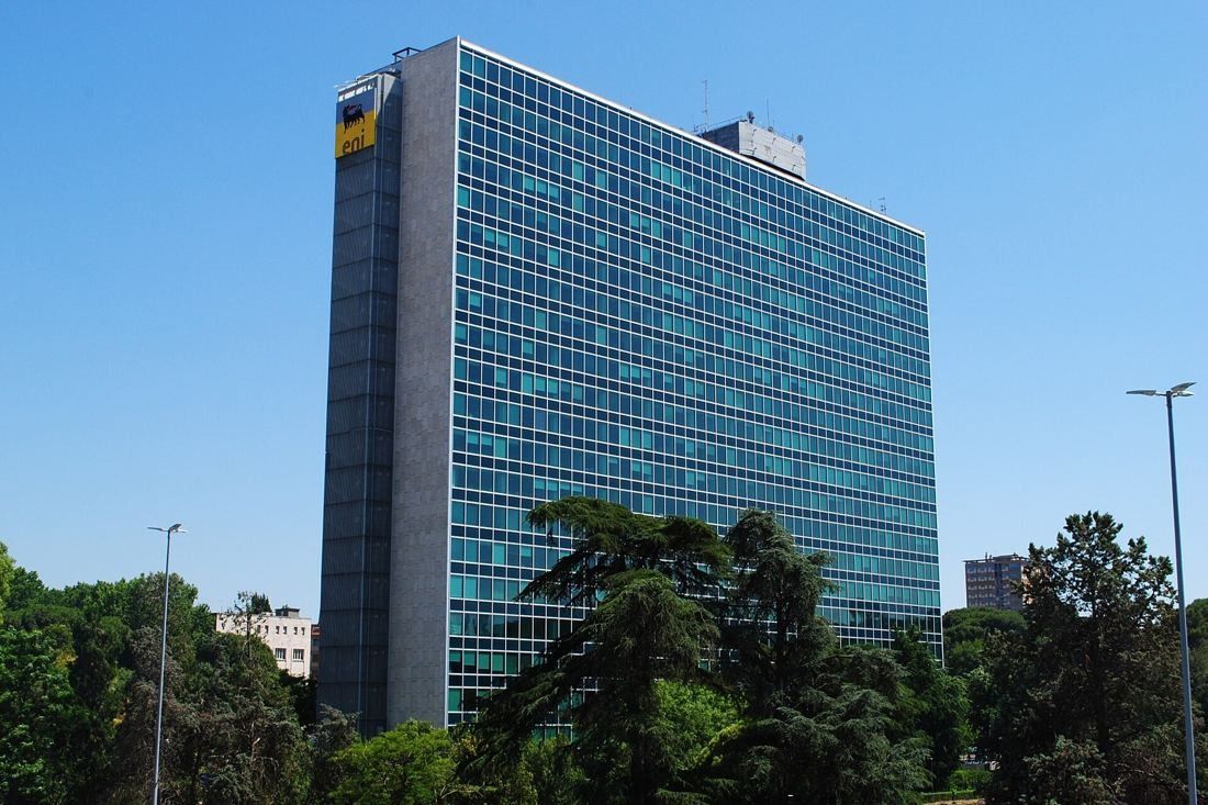 Eni: A glass curtain-wall tower with a stone-clad end wall against a blue sky