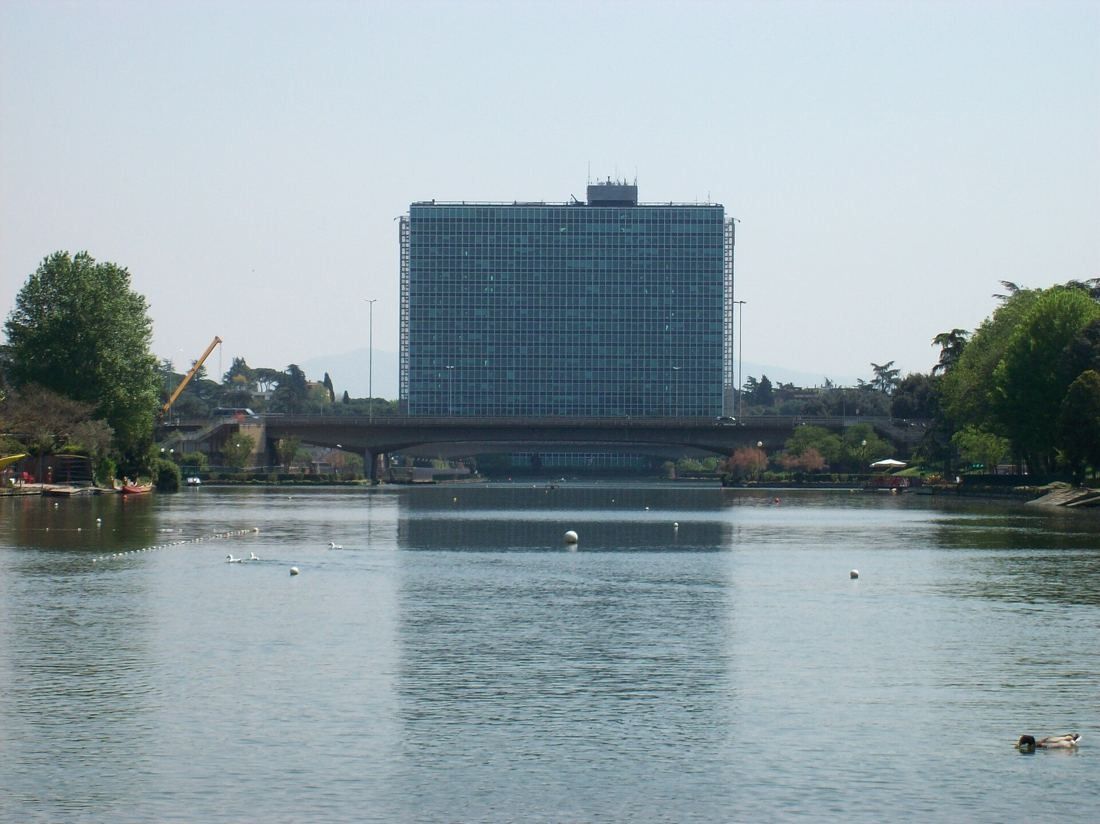 Eni: A glass office slab seen at the far end of a long lake behind a bridge