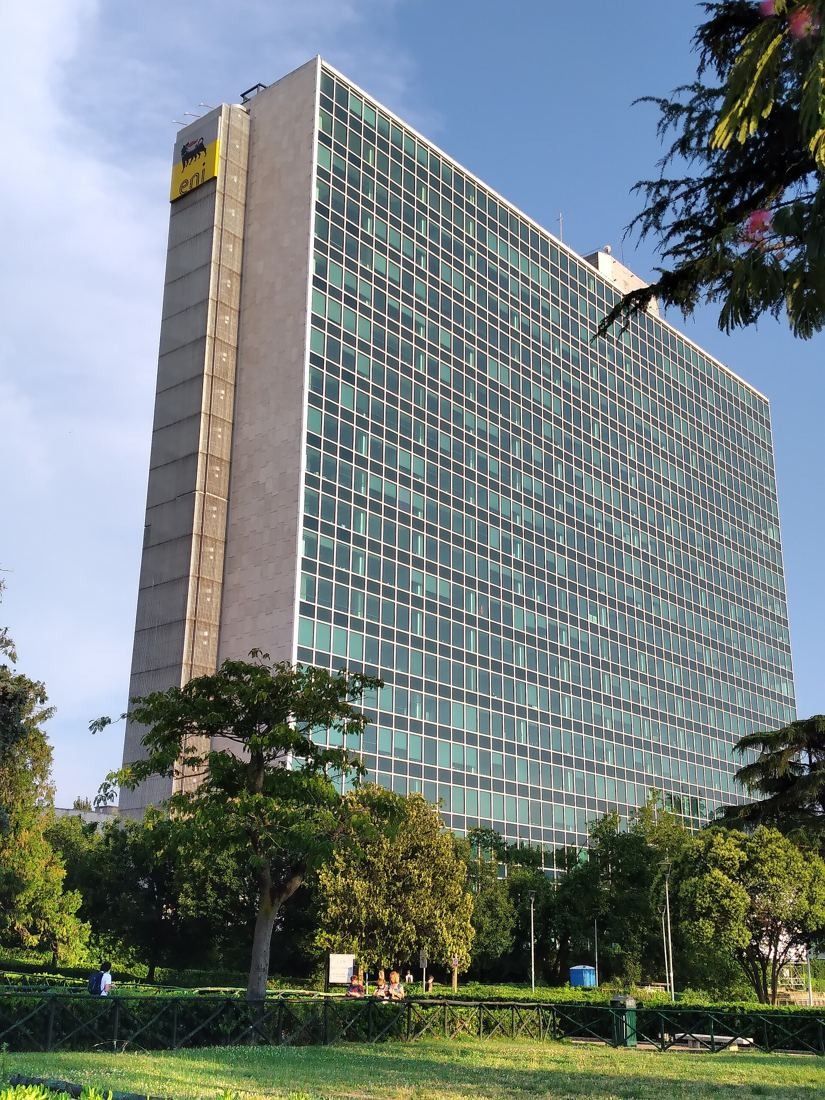 Eni: A glass office tower behind trees and a lawn, framed by flowering branches