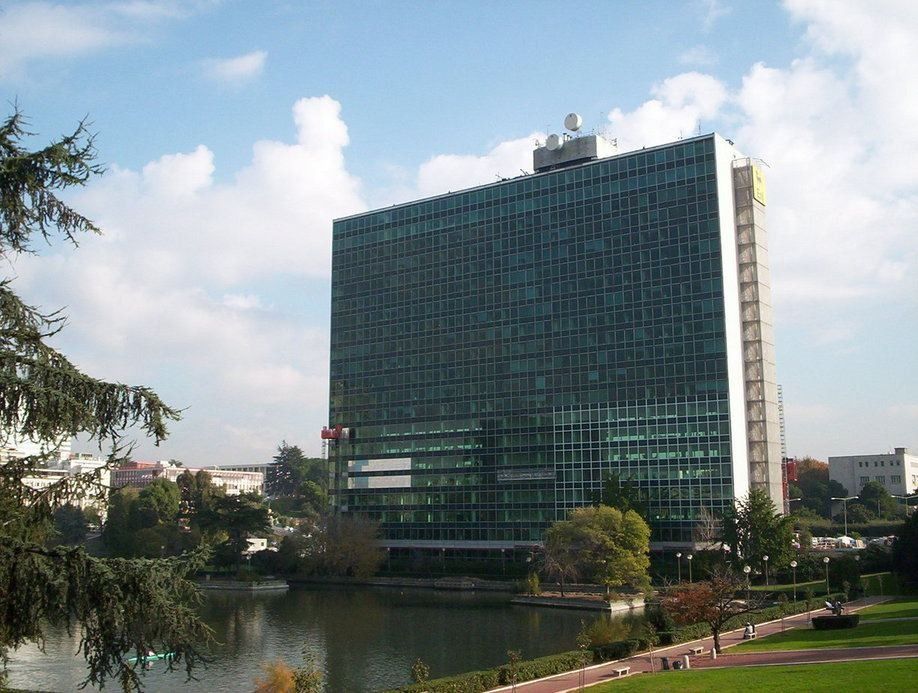 Eni: A glass office tower with a pond and lawn in front under a cloudy sky
