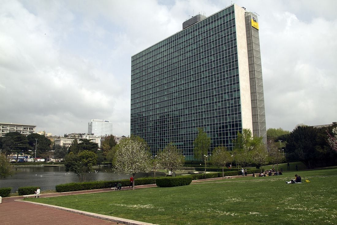 Eni: A glass office tower with stone-clad end walls above a lawn and park paths