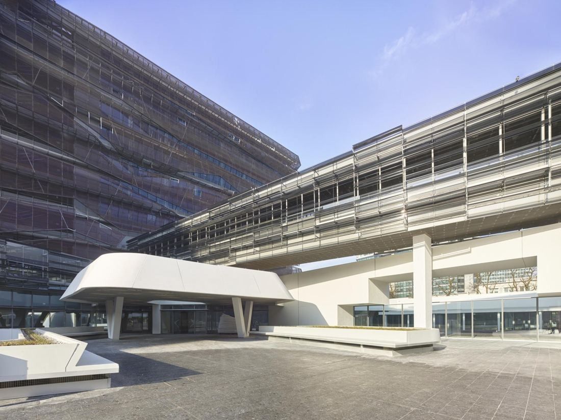 Eni: A long elevated bridge between glass office blocks over a paved plaza