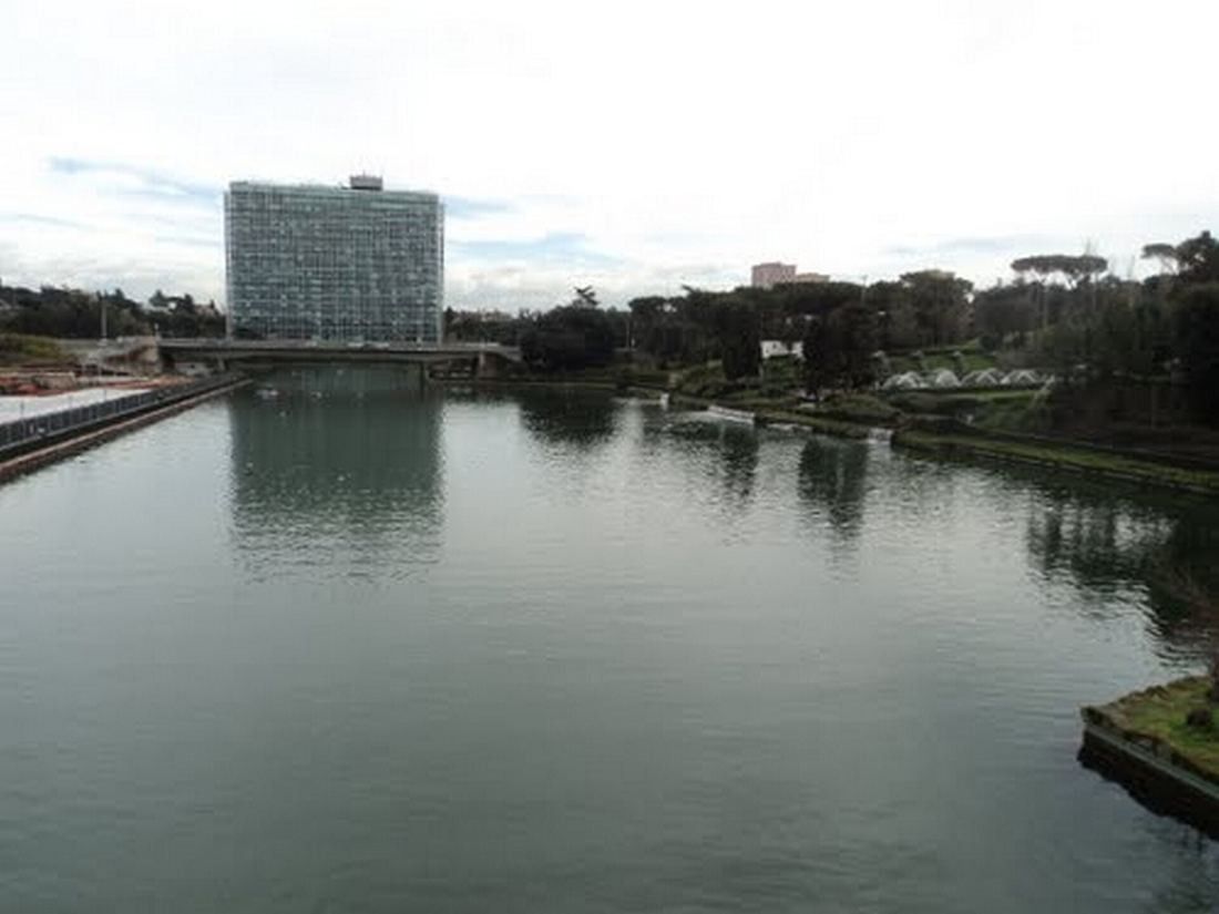 Eni: A long lake leading toward a glass office tower in the distance