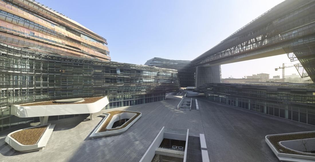 Eni: A raised steel bridge crossing between office blocks above a paved piazza
