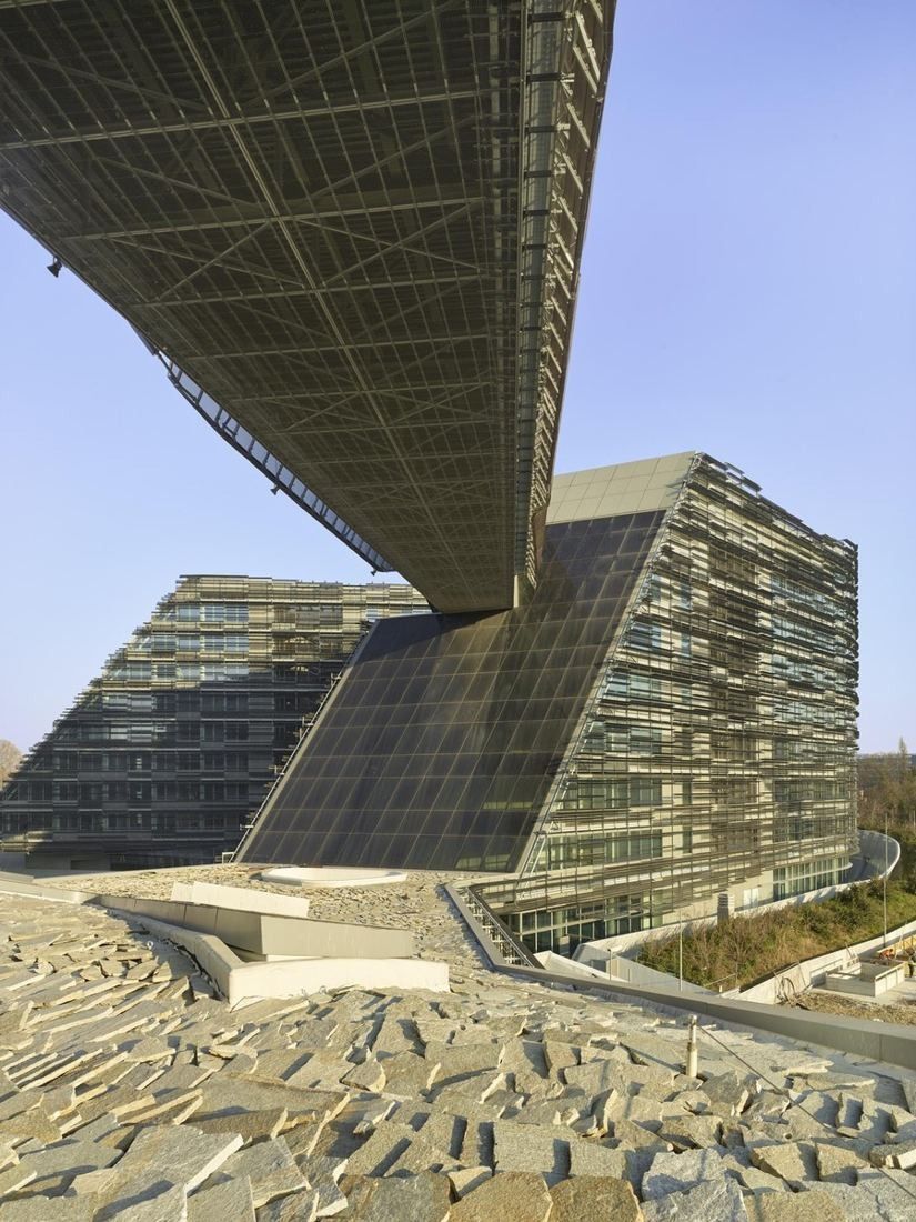 Eni: A sloping office tower under a large overhanging structure seen from below