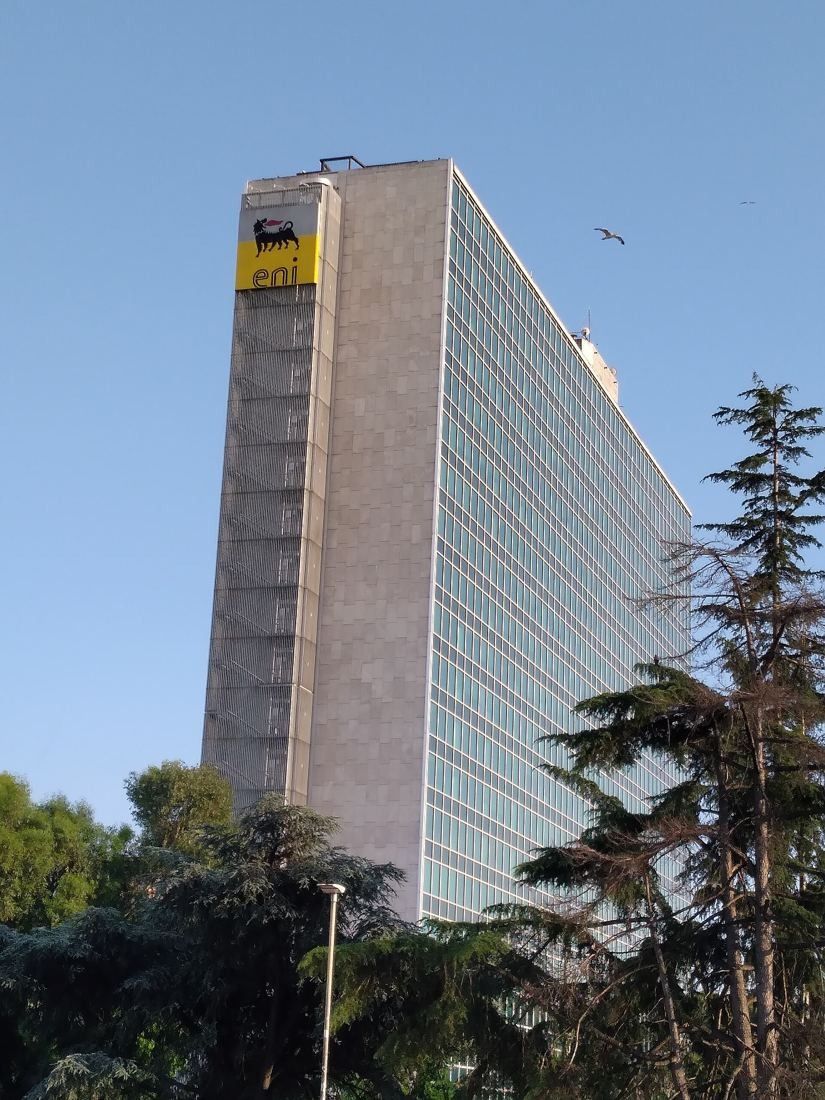 Eni: A tall stone end wall and glass facade rising above trees