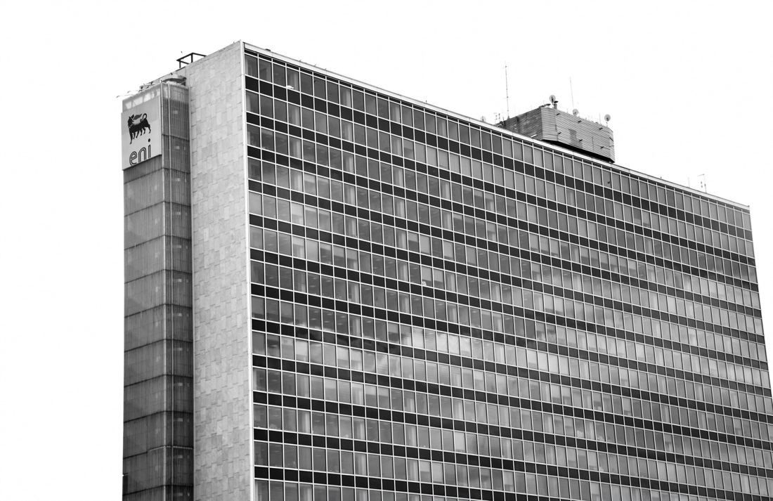 Eni: Black-and-white view of a gridded glass facade and a stone end wall