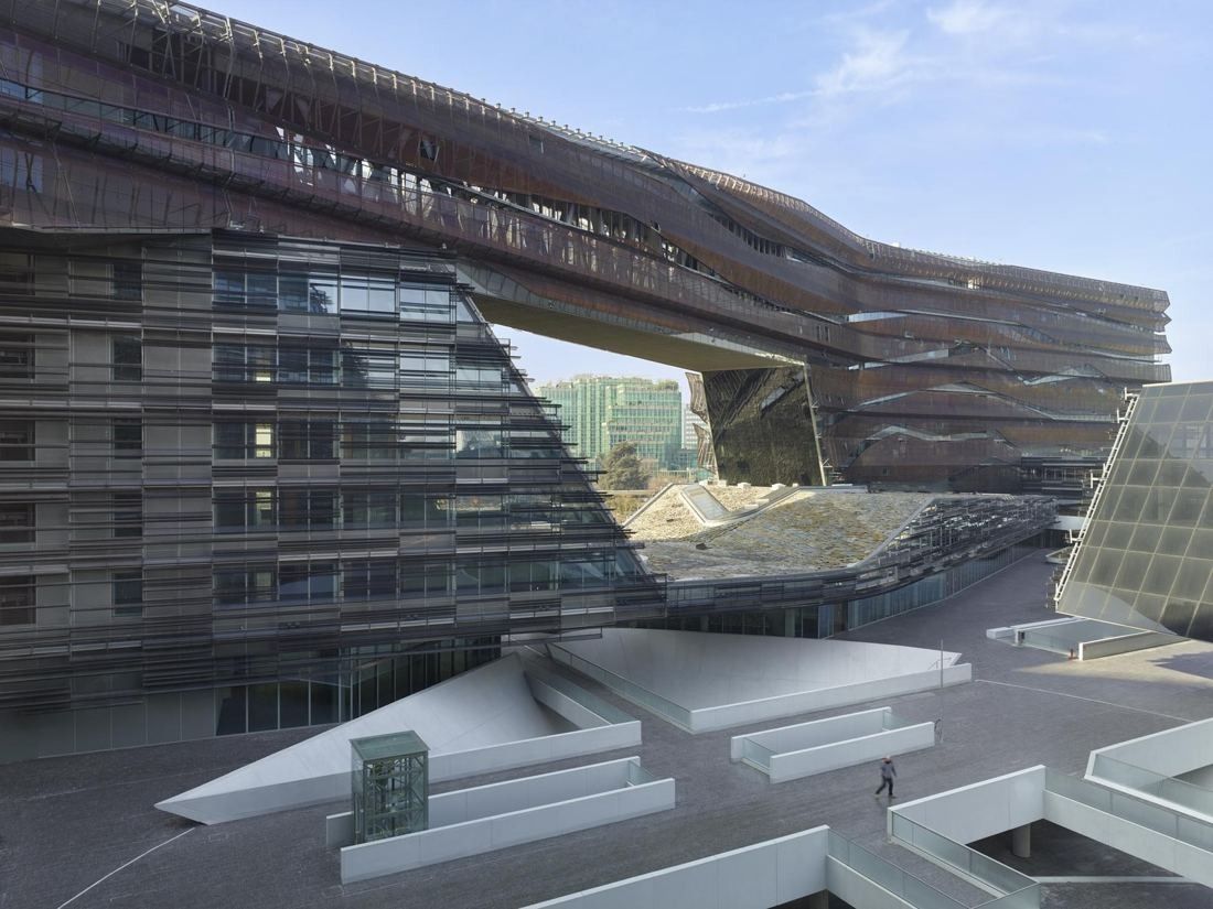 Eni: Office blocks with layered metal facades wrapping around a stepped stone courtyard