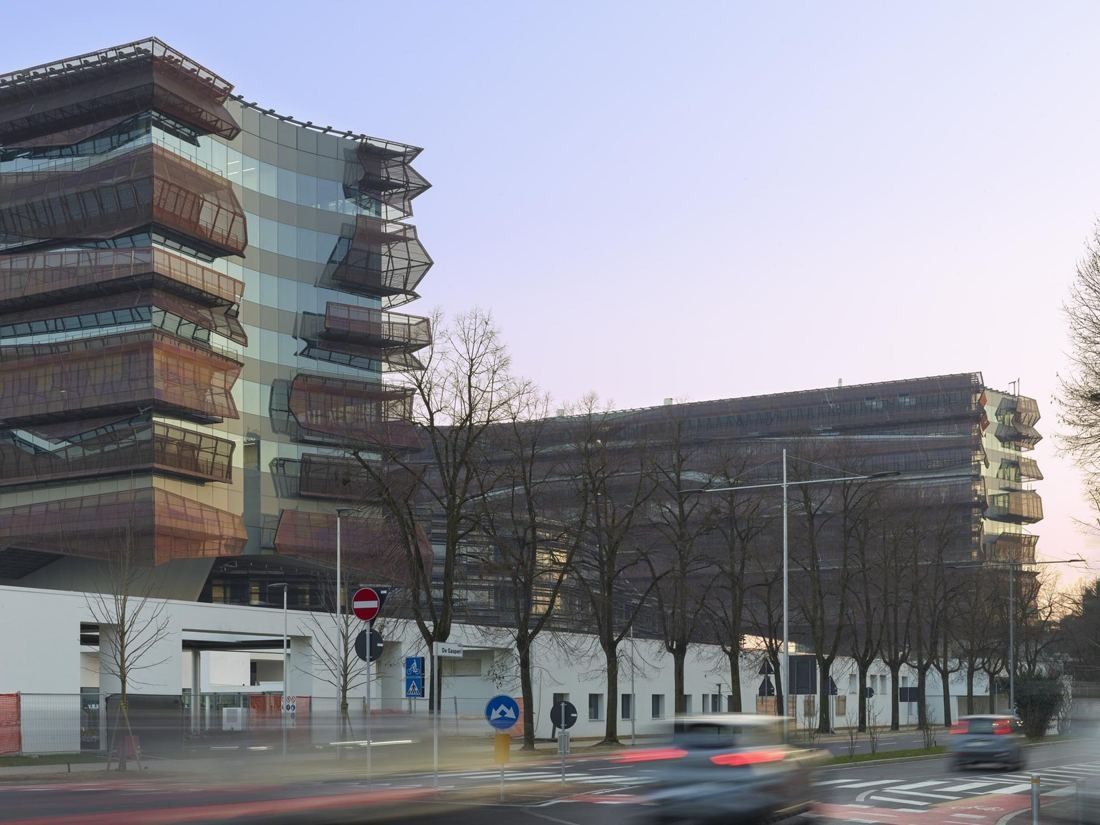 Eni: Office blocks with stacked bronze-toned bands behind a tree-lined street