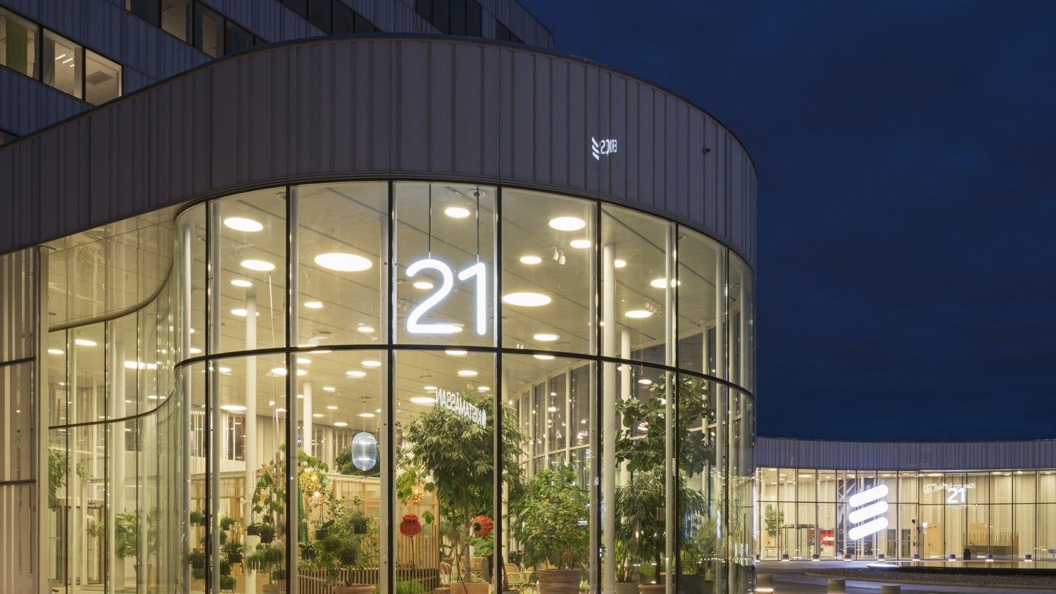Ericsson: Lit round glass entrance hall with plants and the number 21 at night