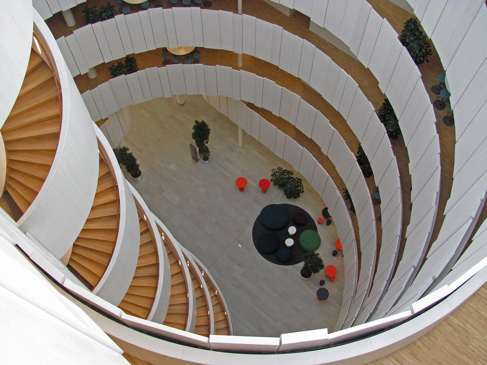 Ericsson: View down a round stairwell with curving white balustrades to a lobby floor with plants