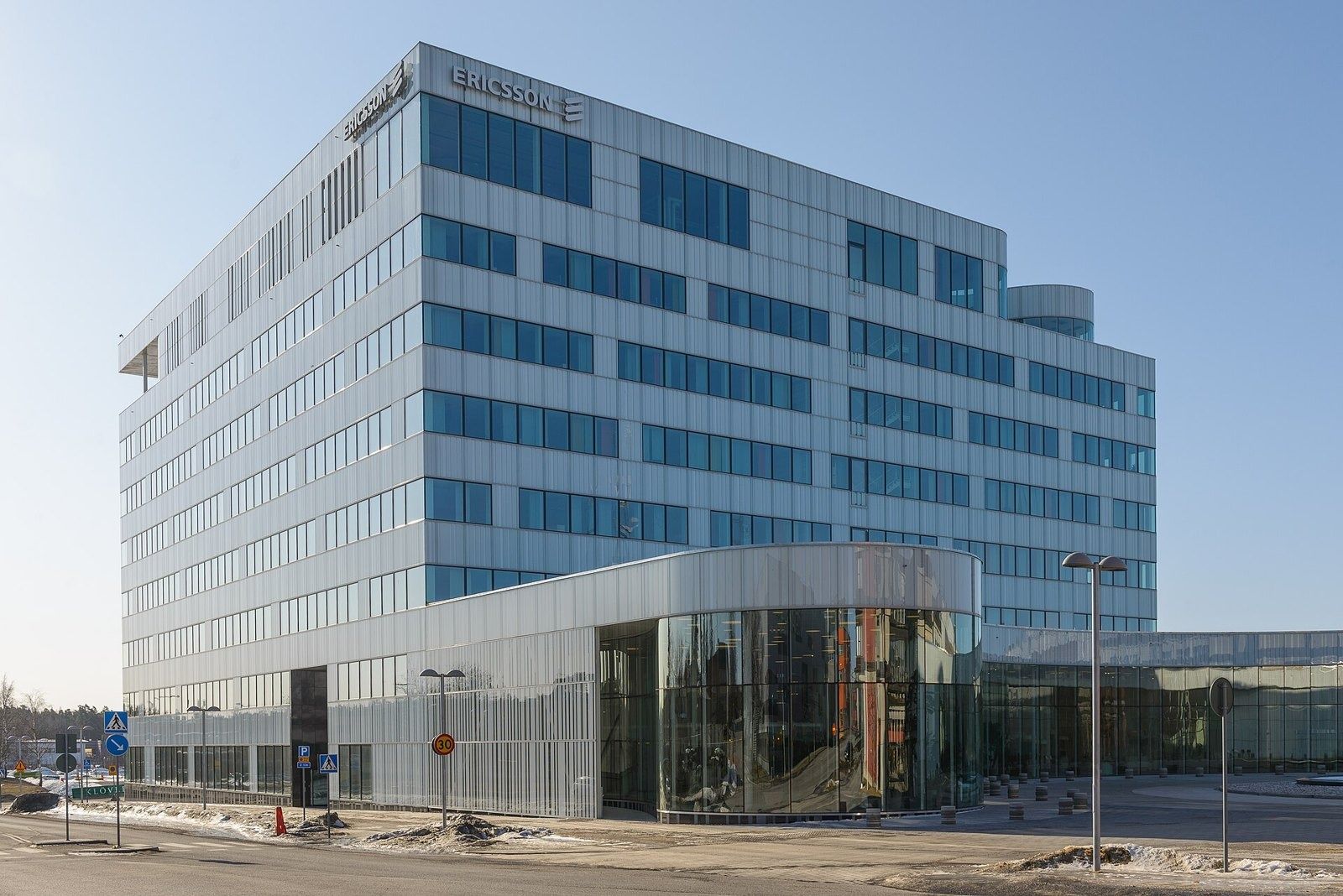 Ericsson: White office building with a curved glass base, young trees and a round pond