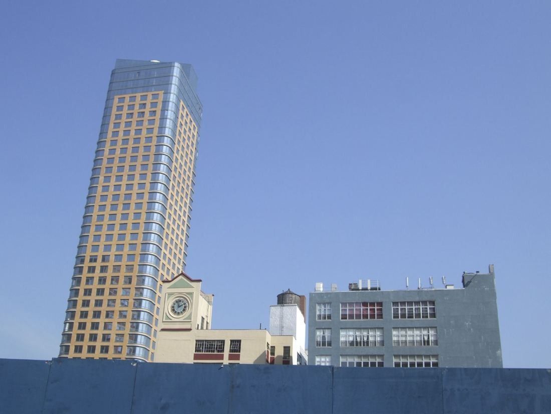 Small clock tower on a brick building with a tall residential tower behind