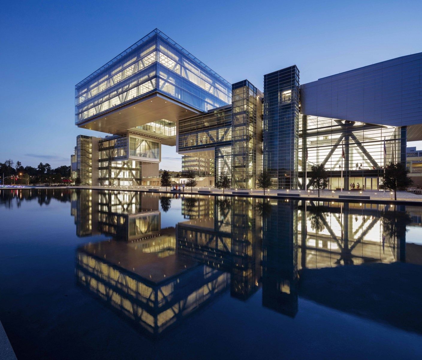 Glass building with a floating box on top reflected in a pond at night